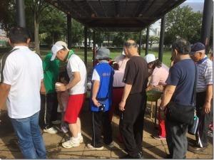 運動着姿の男女が休憩の時のお茶やお菓子を一列に並んで取っている様子の写真